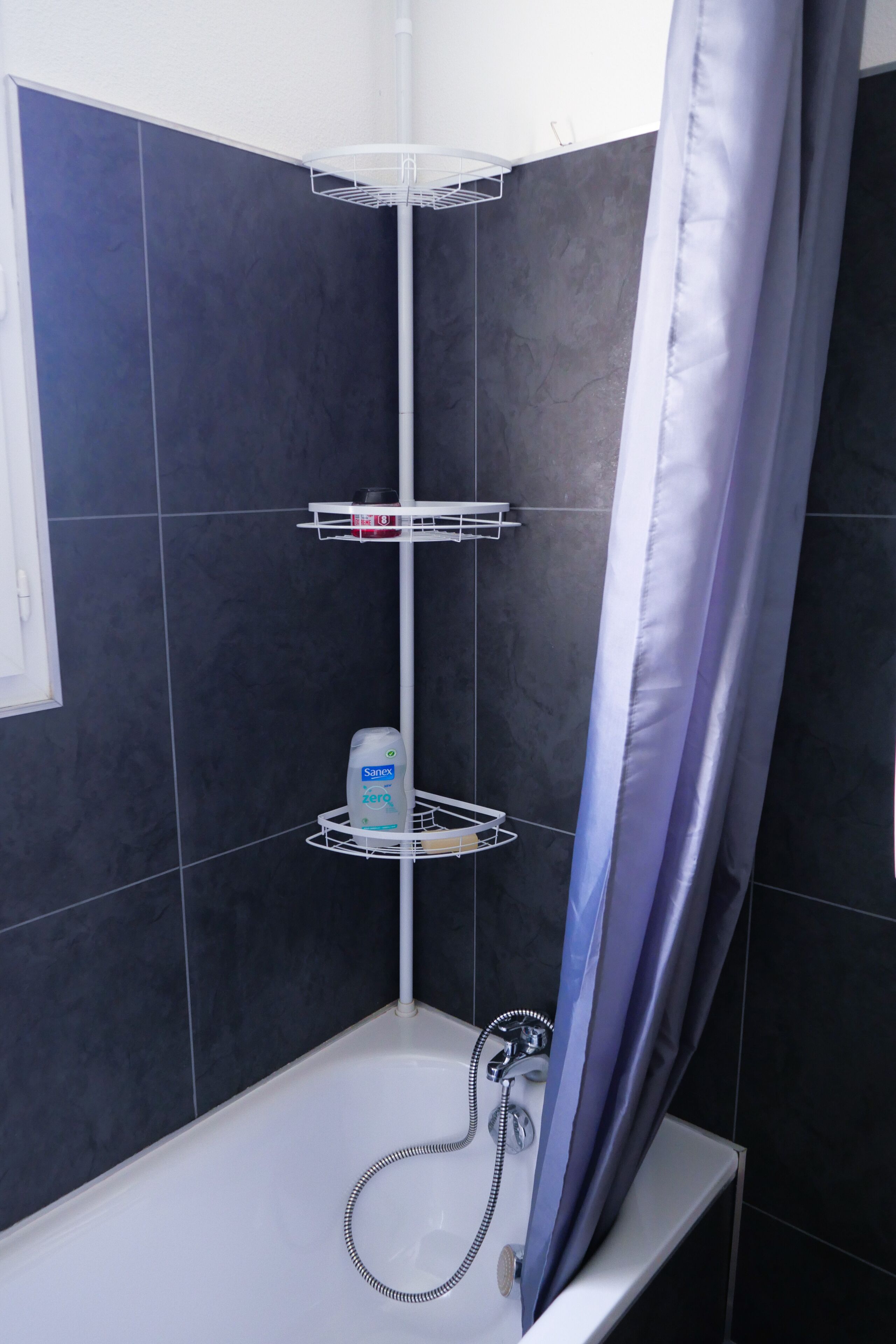 Un área de ducha con una bañera blanca, un cabezal de ducha y un estante con artículos de aseo.