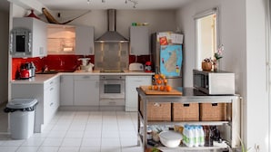 Une cuisine moderne avec des armoires blanches, une hotte en acier inoxydable, un appareil électroménager rouge et un réfrigérateur orné d’une carte du monde.