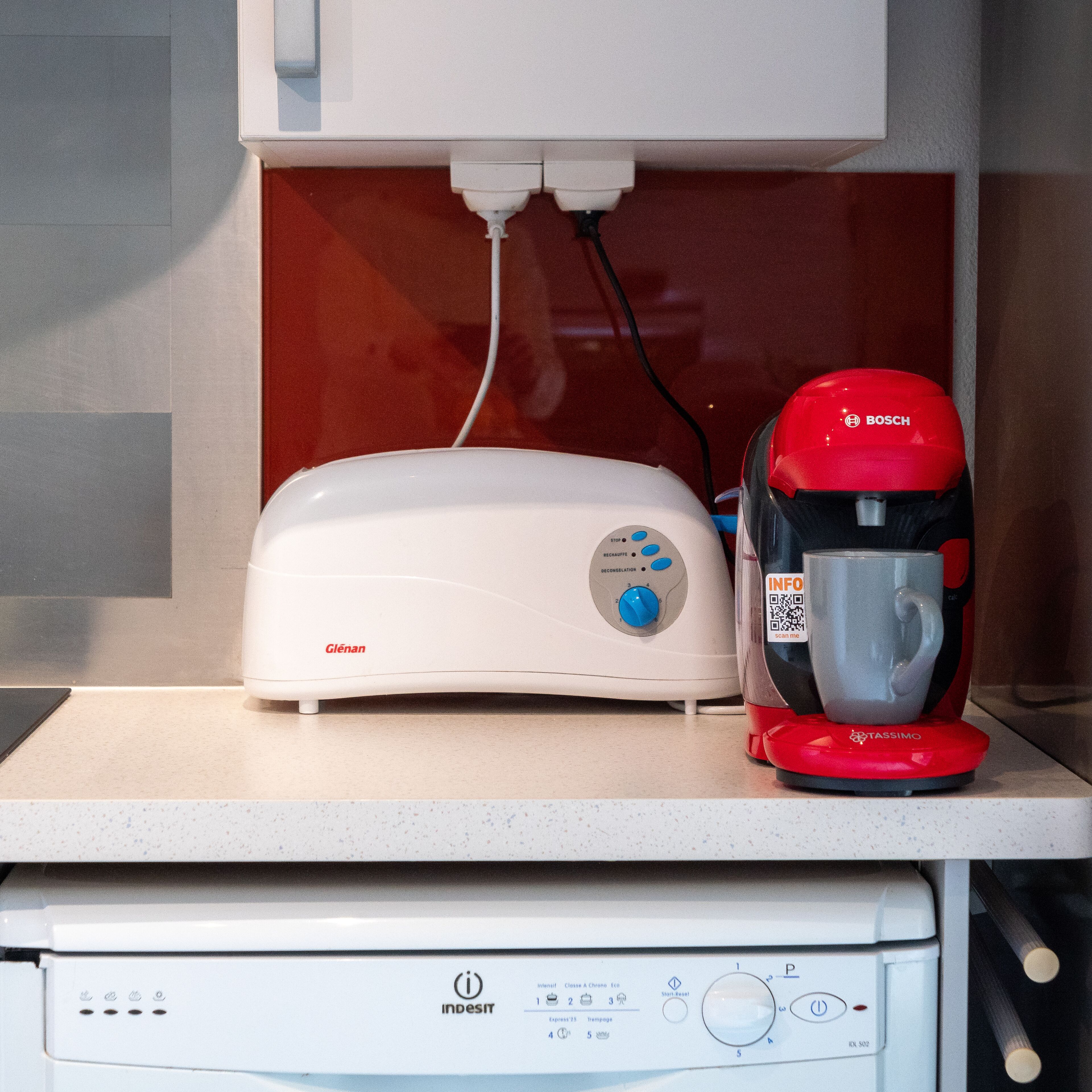 Une cuisine avec un grille-pain blanc, une cafetière rouge et un four à micro-ondes blanc.
