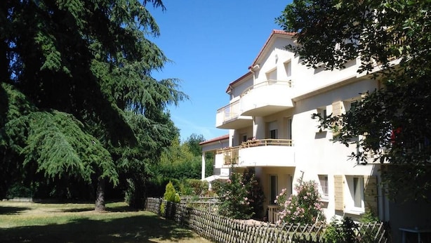 Un bâtiment à deux étages doté de balcons, entouré d’arbres et d’un mur de pierre.
