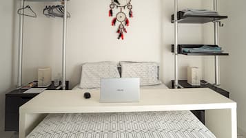 A modern bedroom with a bed, a desk with a laptop, a dreamcatcher, and storage shelves.