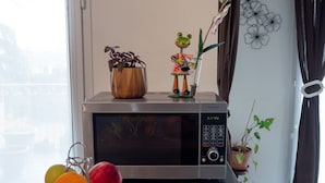 Une cuisine équipée d’un four à micro-ondes, d’un présentoir à fruits et d’un saladier rempli d’oranges posé sur le comptoir.