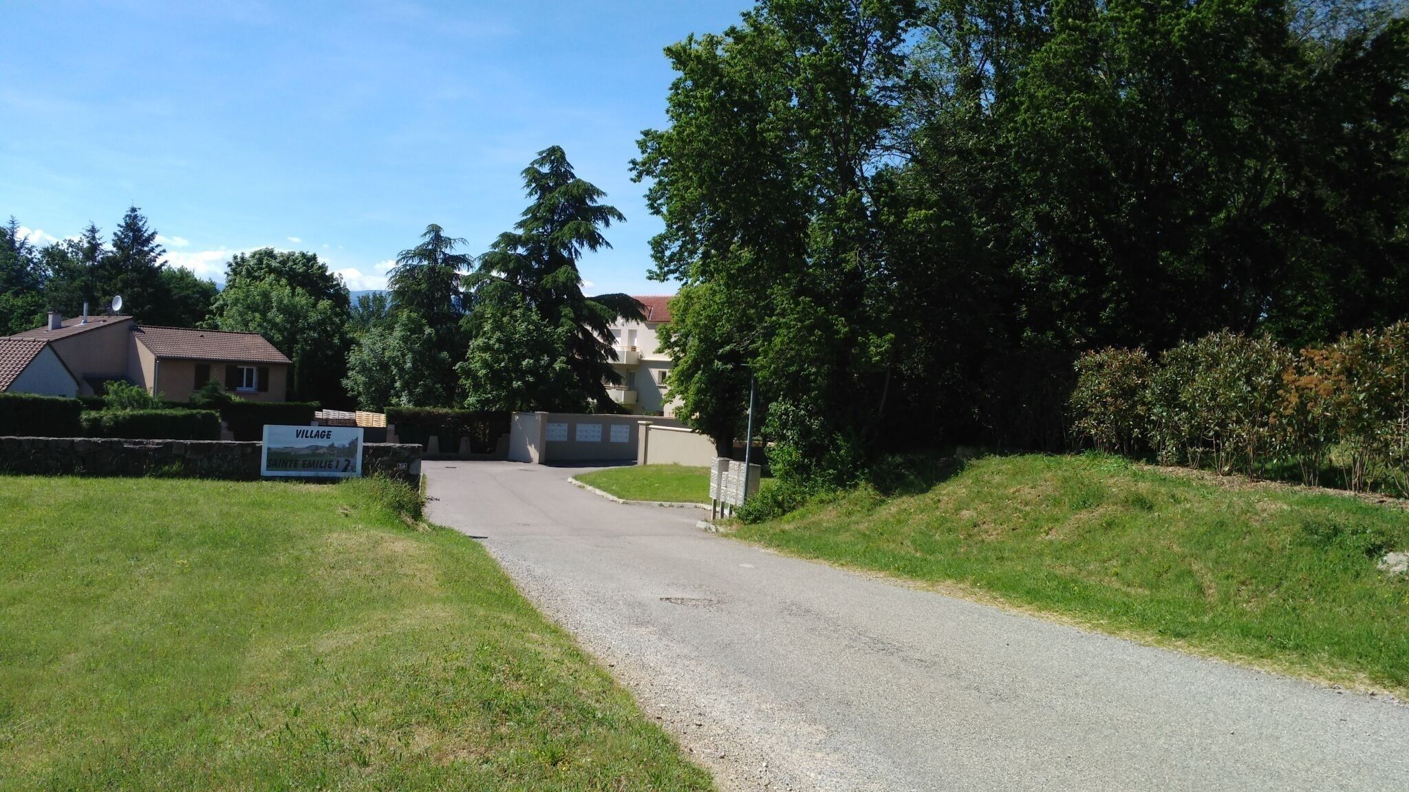 Camino rural que conduce a una entrada con portón y un cartel que indica un pueblo.