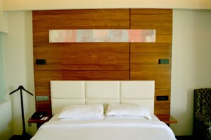 A hotel room with a wooden headboard, a bed with white linens, a bedside table with a phone, and a patterned armchair.