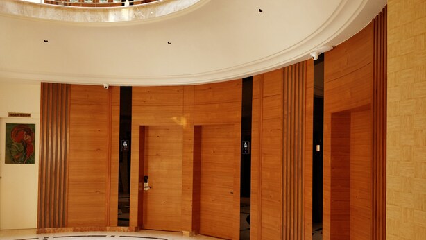 Spaziosa hall con ascensore centrale, pannelli in legno e pavimento in marmo.