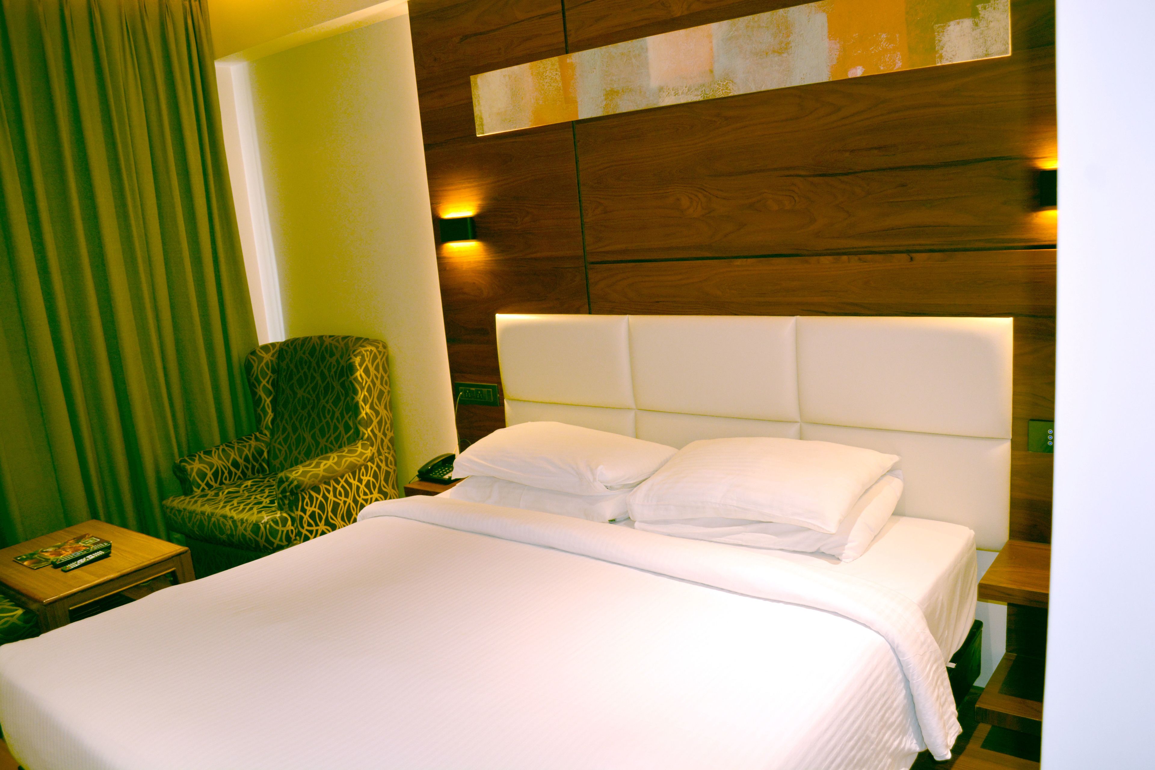A hotel room with a large bed, a patterned armchair, a bedside table with a phone, and a wall-mounted light fixture.