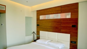 Una moderna camera d'hotel con un grande letto, una testiera in legno e un comodino con telefono e telecomando.