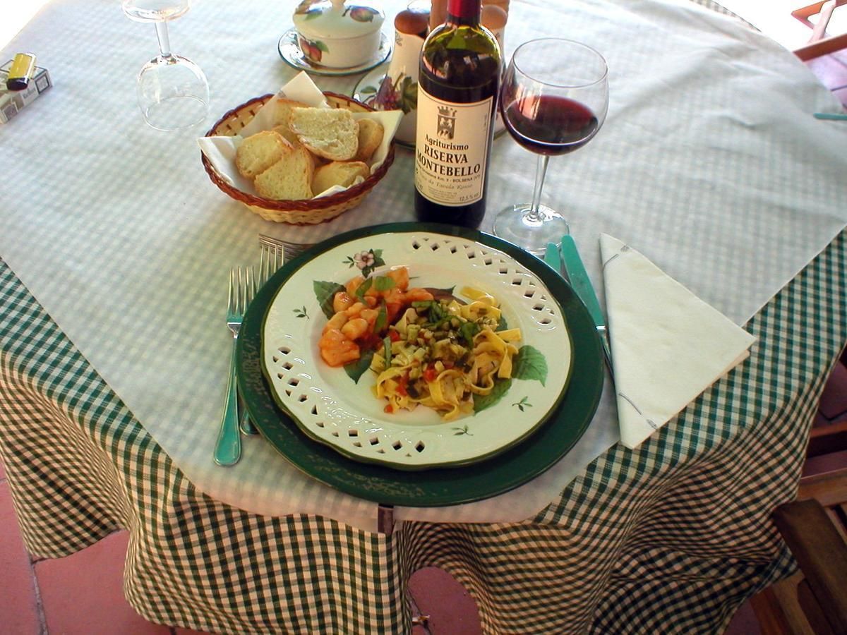 Une table dressée avec une assiette de pâtes, une bouteille de vin et un panier de pain.
