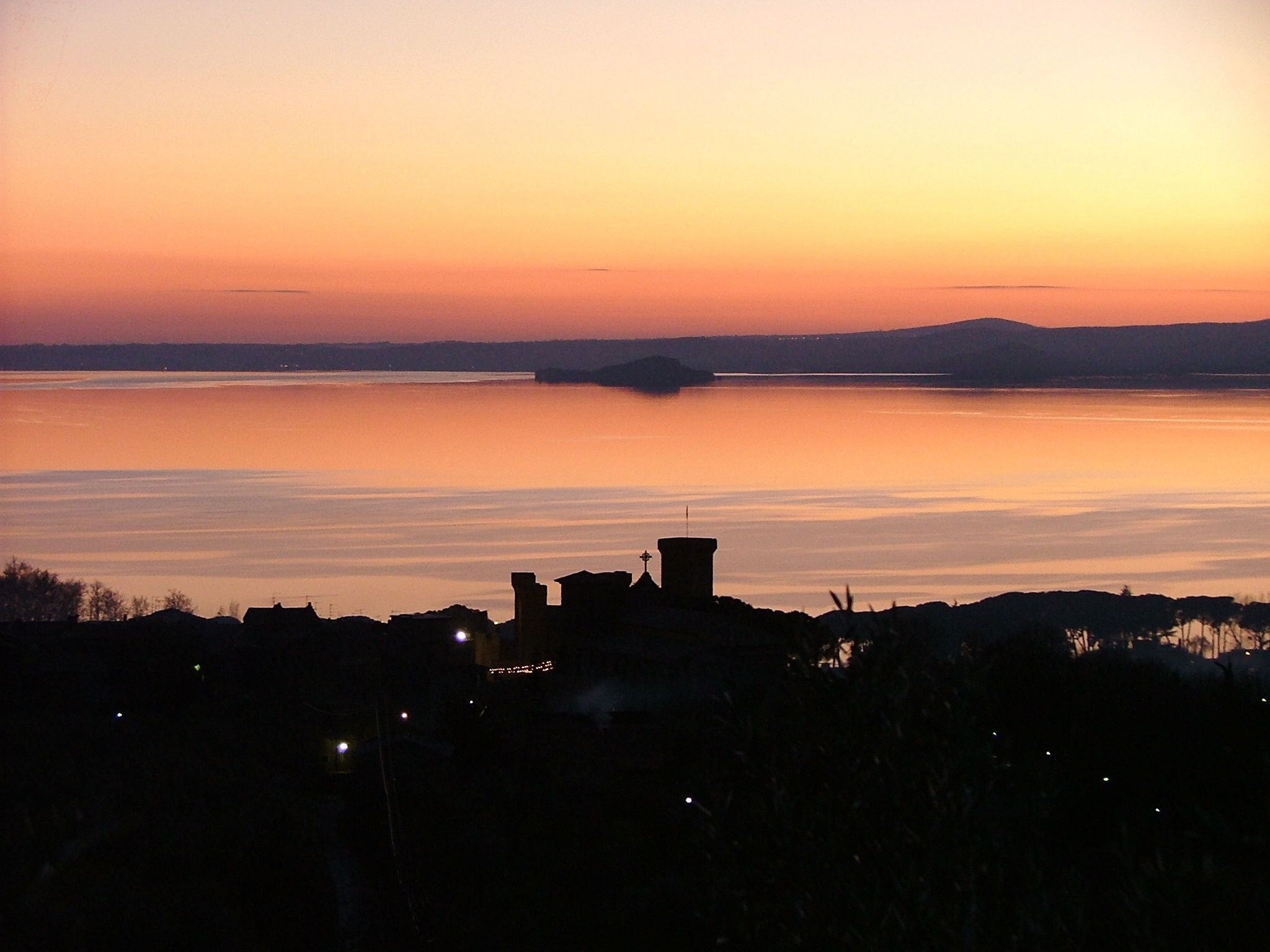 Una vista al atardecer sobre un cuerpo de agua tranquilo, con la silueta de una costa distante.