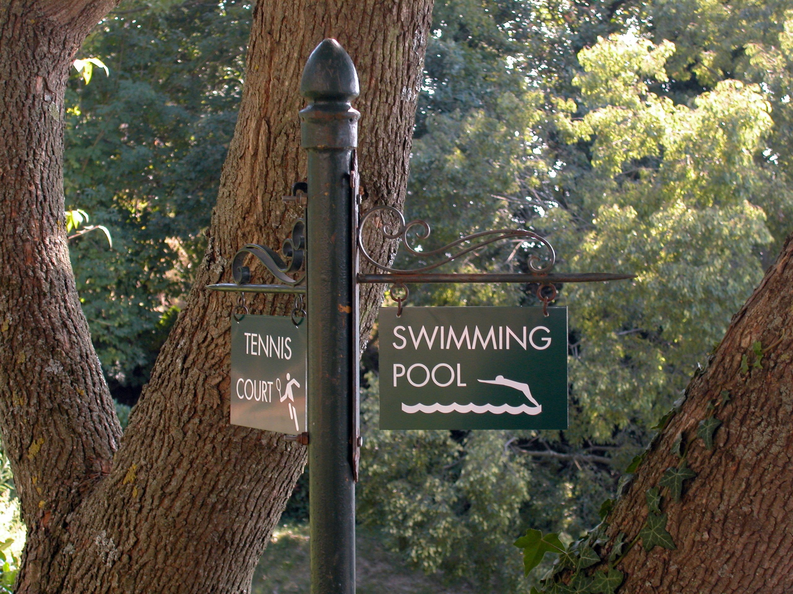 A signpost with two signs: one for a tennis court and another for a swimming pool.