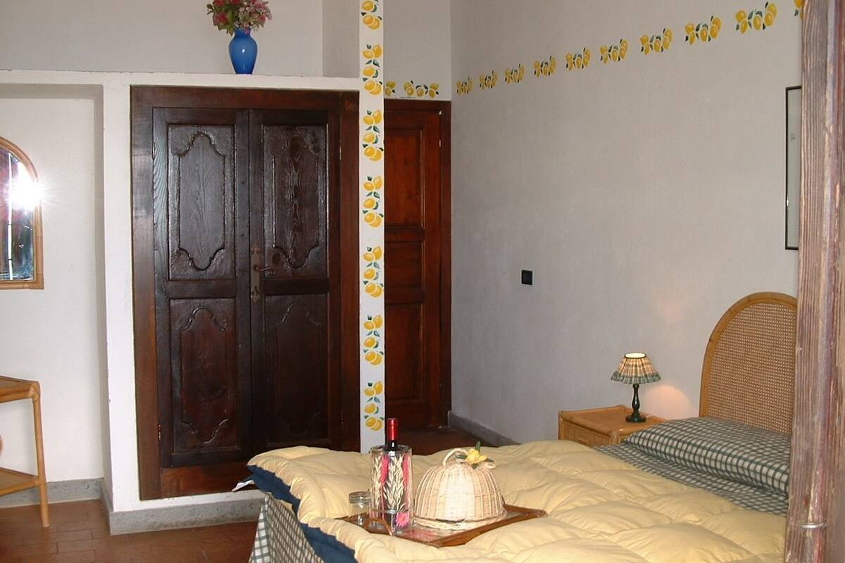 A bedroom with a bed, a nightstand, a lamp, a vase with flowers, and a wooden wardrobe.