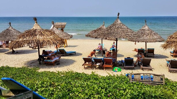 A beach with thatched umbrellas and lounge chairs, a clear view of the ocean, and a sandy beach. - An Bang Scent Beach Homestay (Da Nang)
