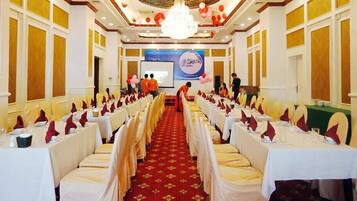 A banquet hall with rows of tables set for a formal event, a stage with a presentation screen, and a chandelier.