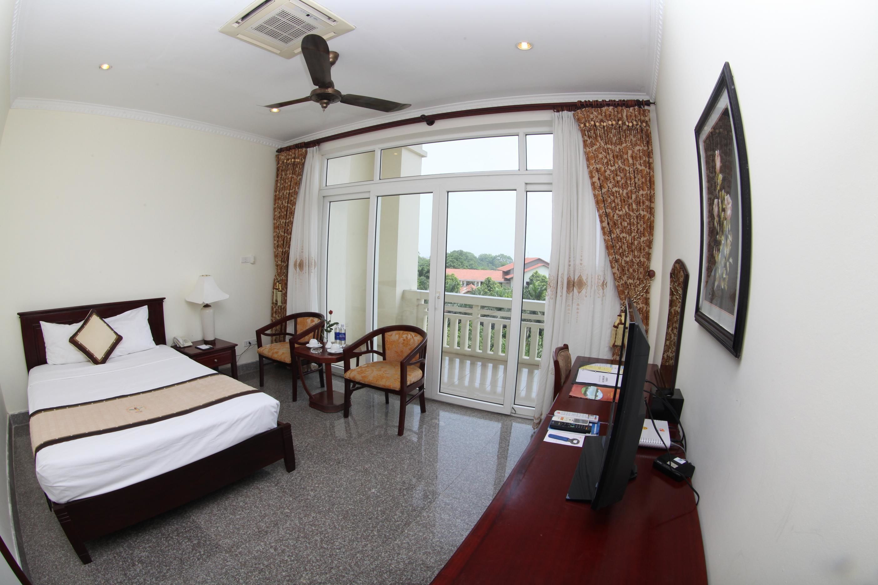 A hotel room with a bed, two chairs, a desk, a television, and a large window with a view of buildings.
