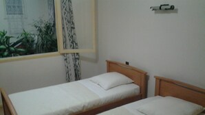 Two single beds with wooden frames and white bedding in a room with a window and a curtain. - Lafayette (Saint Sever)