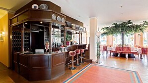 A bar area with a wooden counter, stools, and a wine rack. There is a seating area with tables and chairs in the background. - Hotel Trebeltal (Demmin)