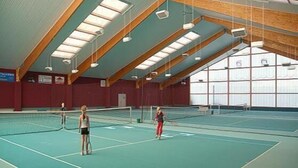An indoor tennis court with a high ceiling and wooden beams, featuring a green playing surface and multiple tennis courts. - Hotel Trebeltal (Demmin)