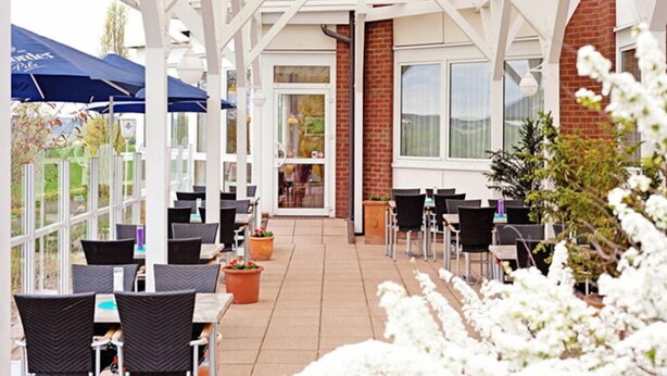 An outdoor patio area with white pergola structures, tables, and chairs. - Hotel Trebeltal (Demmin)