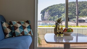 A room with a view of a cliff and beach, a table with a bowl of fruit and bottles, and a blue sofa with patterned cushions. - DAIKYO ENGETSUTO VILLA　 (Shirahama)