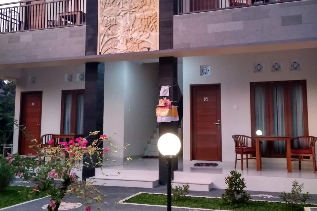 Un edificio de dos plantas con un balcón, un muro decorativo y un jardín cuidado.