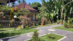A well-maintained garden with a paved pathway, potted plants, and a building with a tiled roof. - Kartika Bungalows (Ubud)