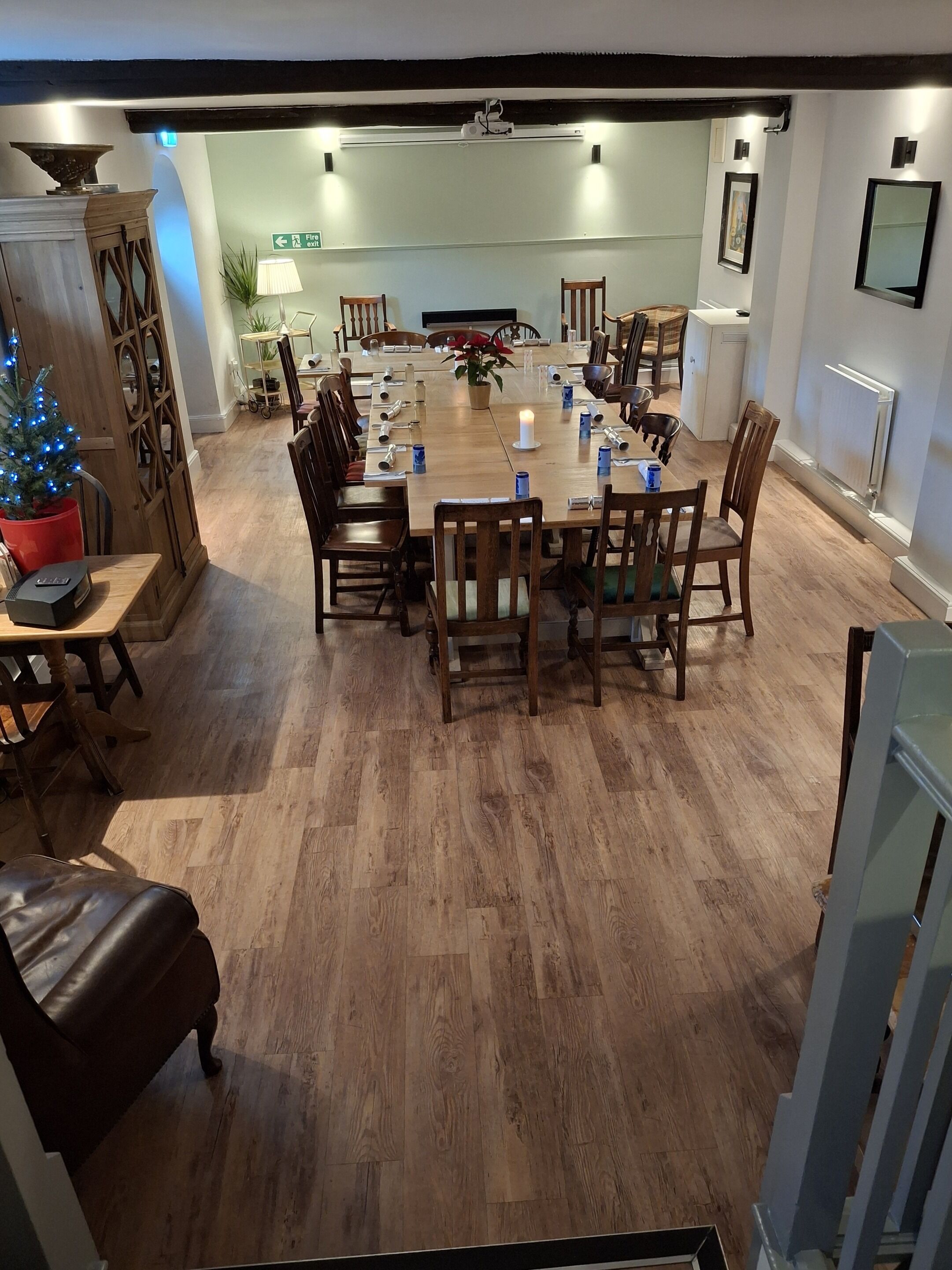 A dining area with a wooden table set for six, surrounded by chairs. A small Christmas tree is visible in the foreground.