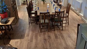 A dining area with a wooden table set for six, surrounded by chairs. A small Christmas tree is visible in the foreground.