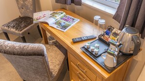 A wooden desk with a remote control, a tray with coffee cups and snacks, and a magazine. - Rose And Crown (Bath)