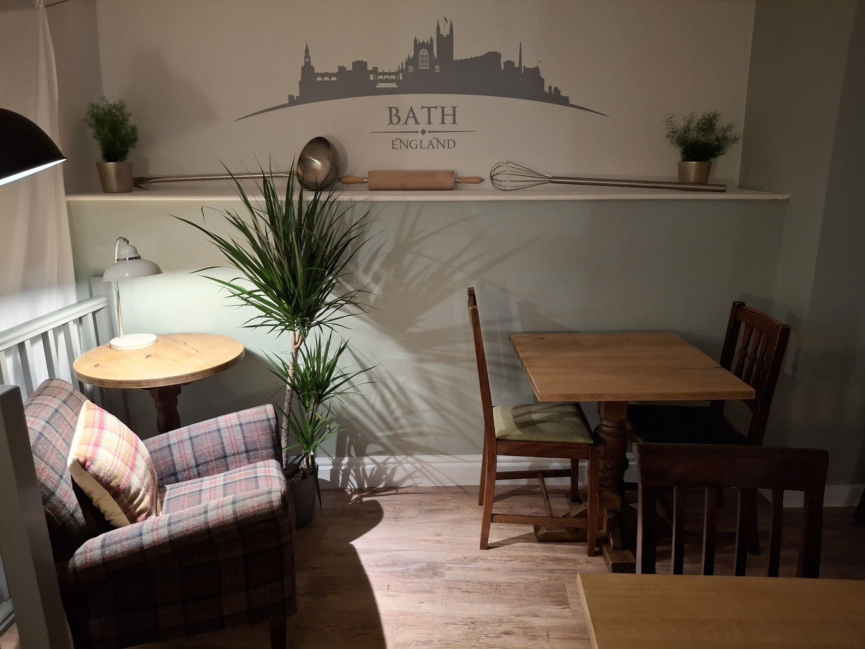 A cozy dining area with a wooden table and chairs, a plaid sofa, a small round table with a lamp, and a wall with a cityscape silhouette.