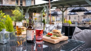 A table with a bottle of Old Moutain Pomegranate cider, a glass of beer, and a burger on a wooden board. - Rose And Crown (Bath)
