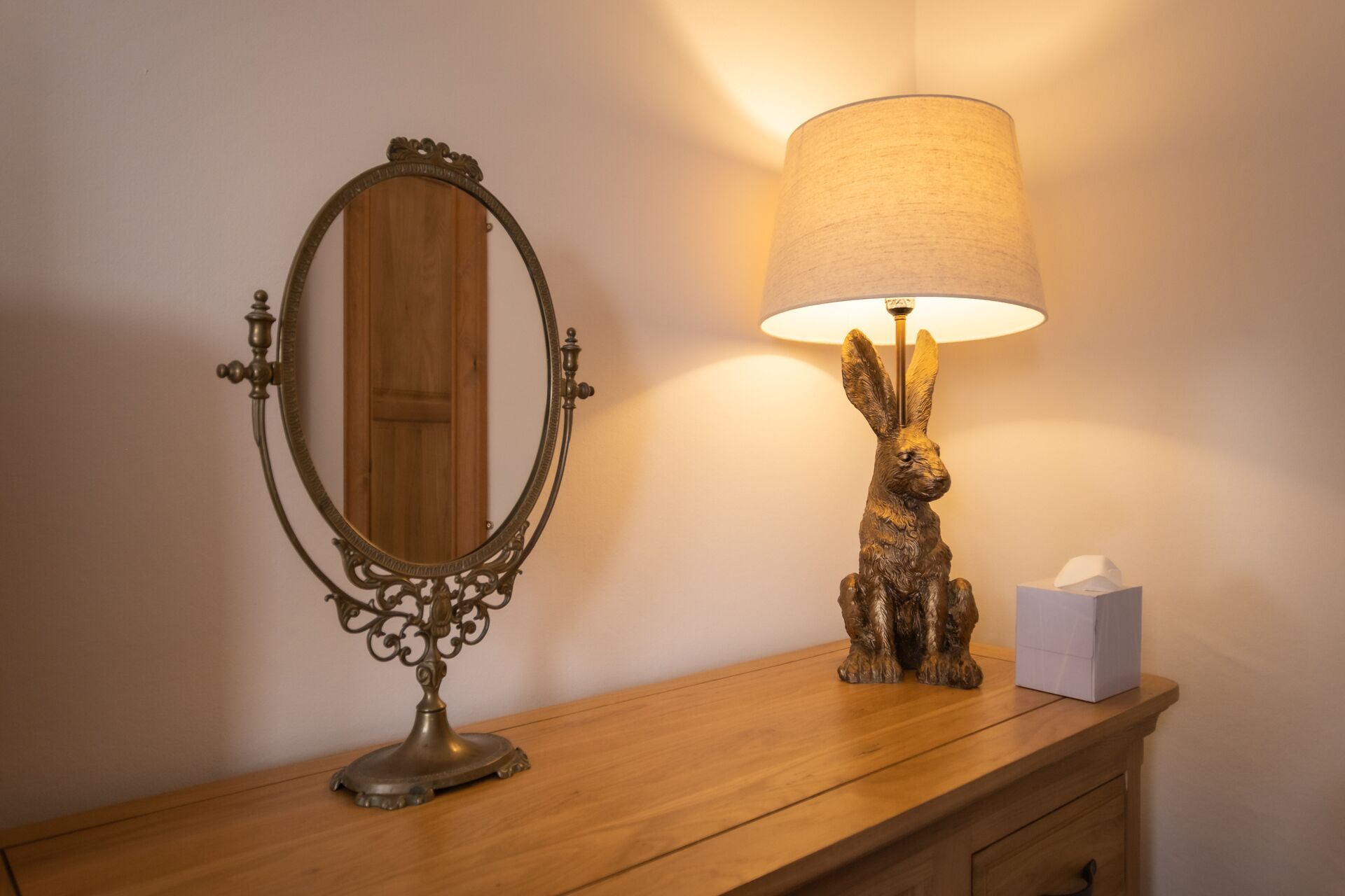 A wooden vanity with a mirror and a lamp with a rabbit figurine.