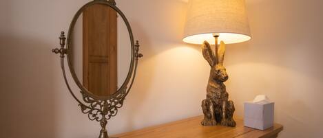 A wooden vanity with a mirror and a lamp with a rabbit figurine.