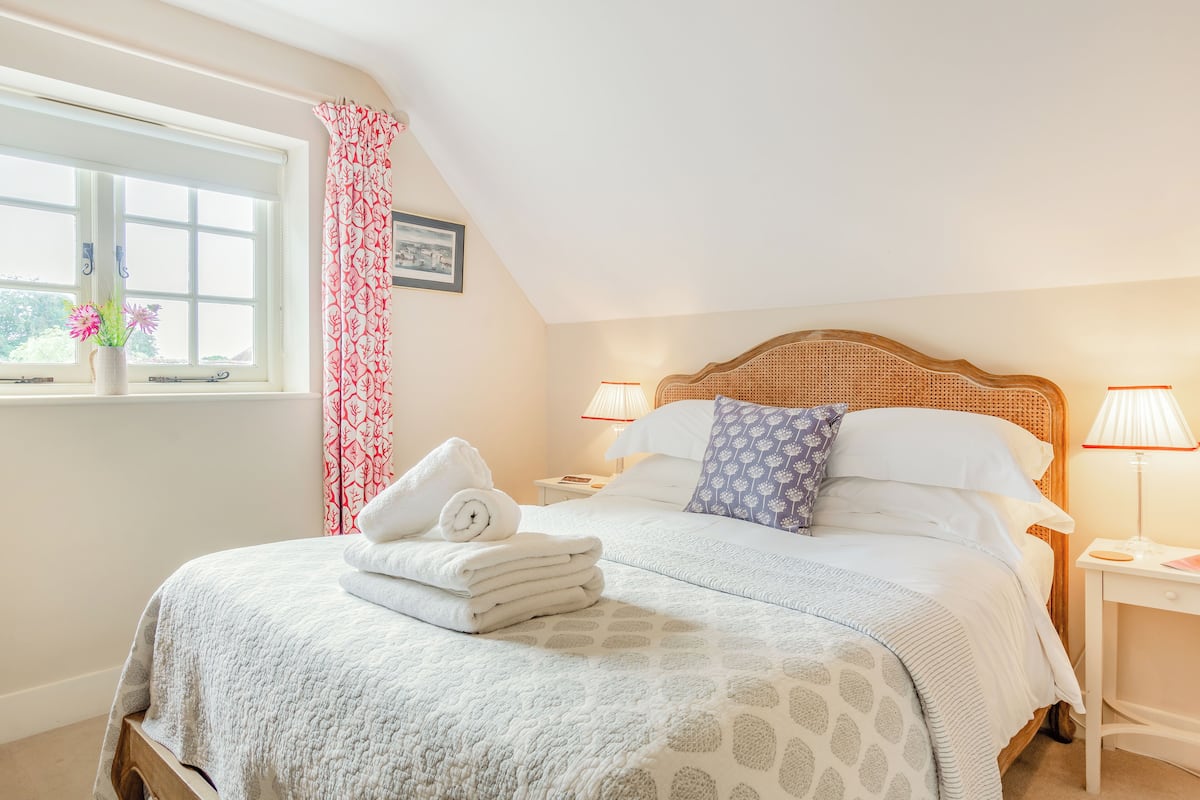 A neatly made bed with a white comforter and pillows, a window with a view, and a bedside table with a lamp.