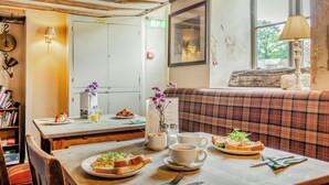 Un coin repas avec une table en bois mise pour le petit-déjeuner, un canapé et une fenêtre donnant sur un beau paysage.