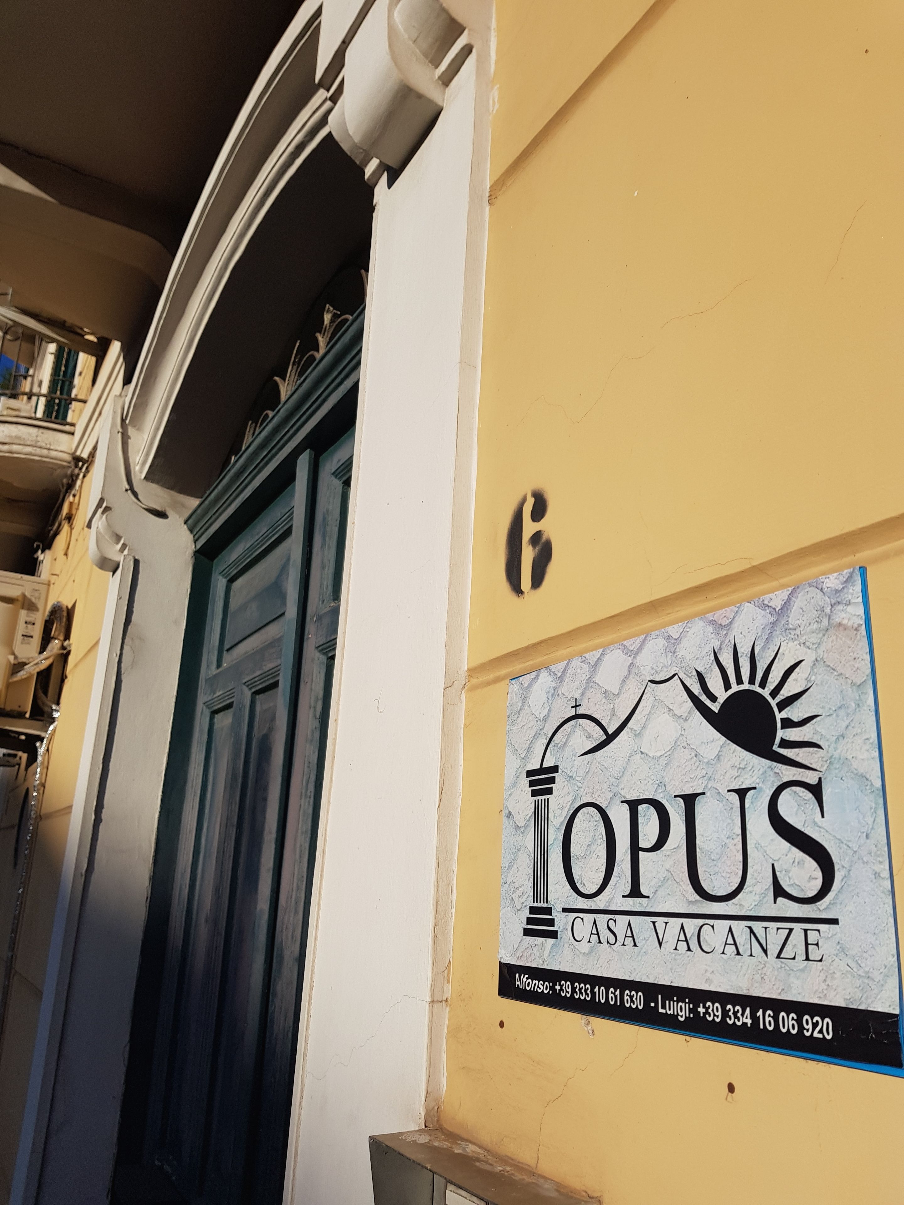 Un edificio con una porta blu e un cartello con la scritta 'OPUS CASA VACANZE' e numeri di contatto.