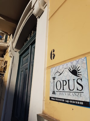 A building with a blue door and a sign for 'OPUS CASA VACANZE' with contact numbers.