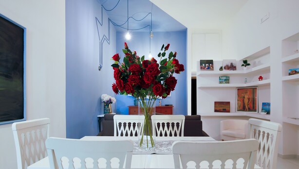 A dining area with a white table and chairs, a vase of red roses, and a blue accent wall. - Opus Casa Vacanze (Pompei)