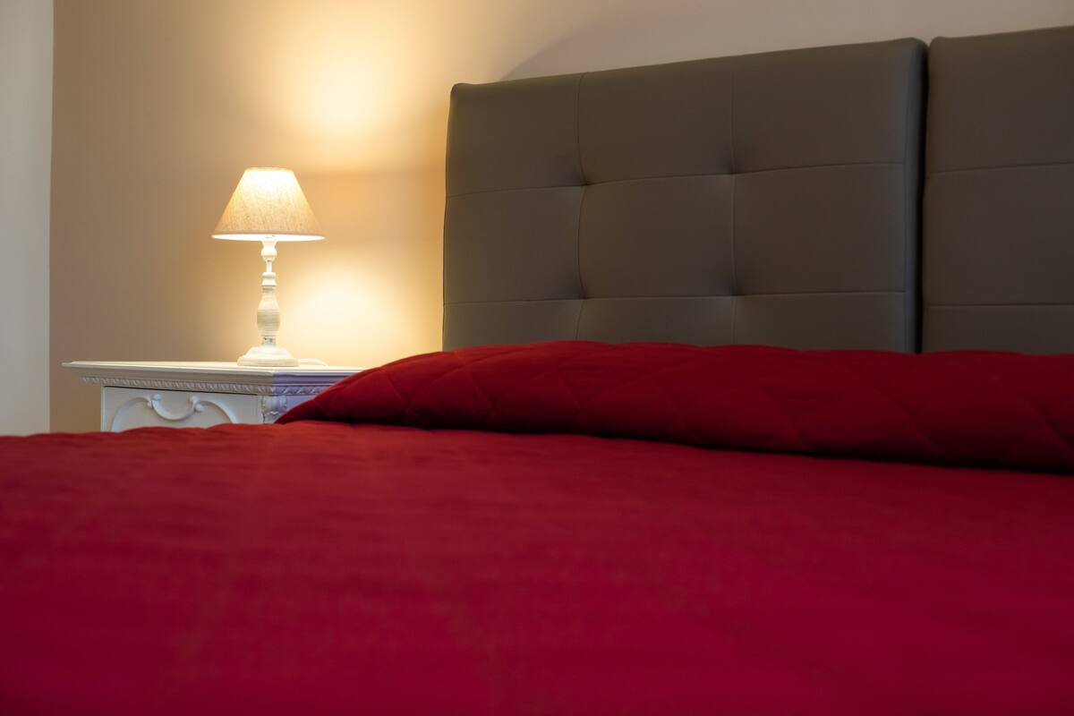 Un lit avec une couverture rouge et une lampe blanche sur une table de chevet.