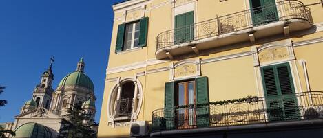 A building with a yellow facade, green shutters, and a balcony with a wrought iron railing.