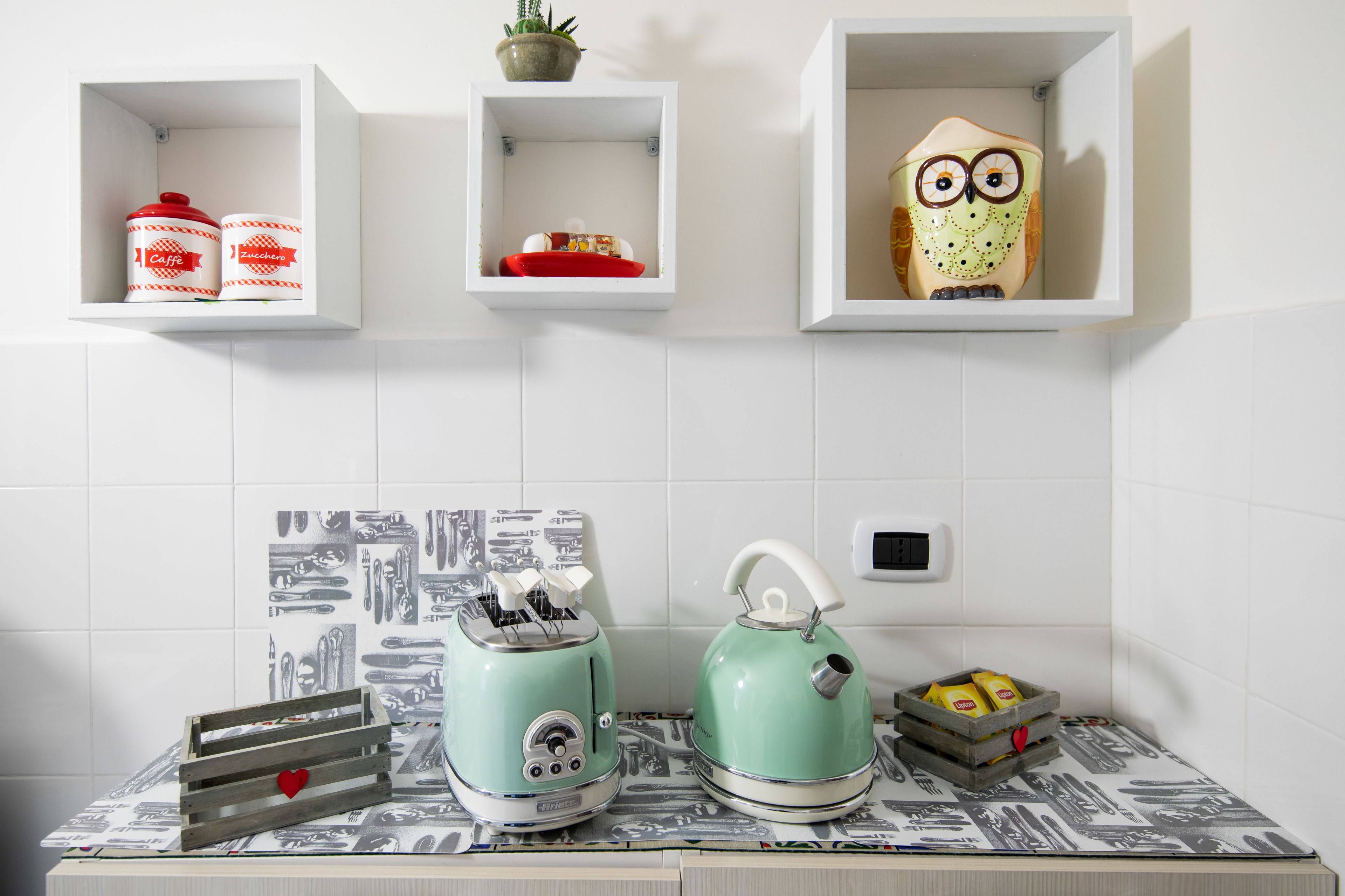 A kitchen with two vintage-style toasters, a kettle, and a small shelf with a decorative owl.