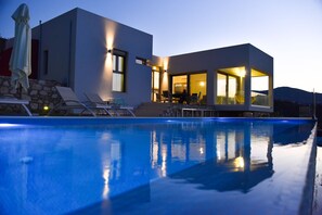 A modern house with a swimming pool, outdoor seating, and a well-lit interior. - Sea View Villas (Malevizi)
