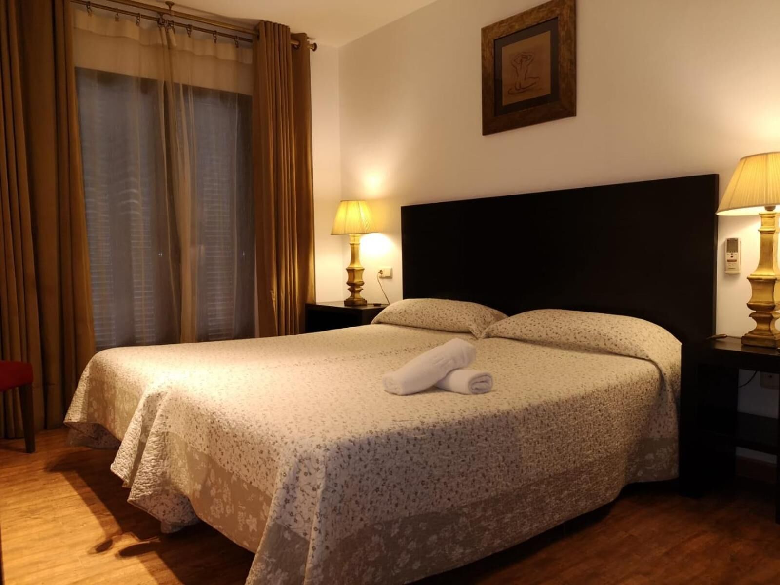 Un lit bien fait, recouvert d’une couvre-lit à motifs floraux, avec deux lampes de chevet et une serviette pliée posée sur le lit.