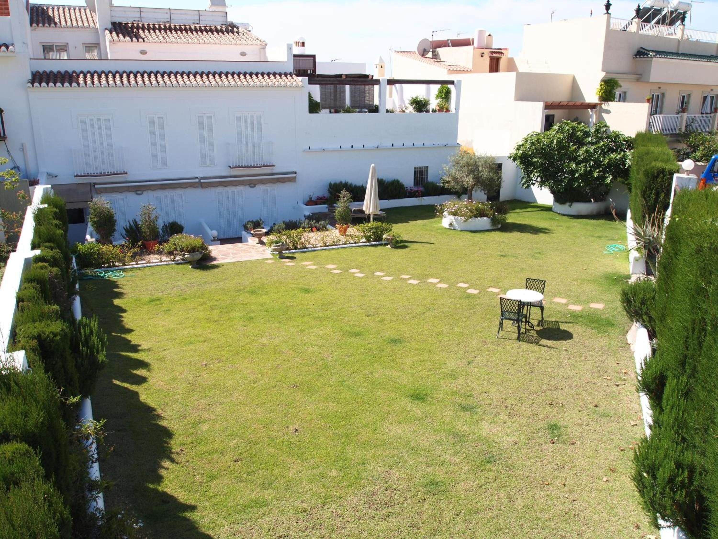 A well-maintained courtyard with a lawn, a small table and chair, and various potted plants.