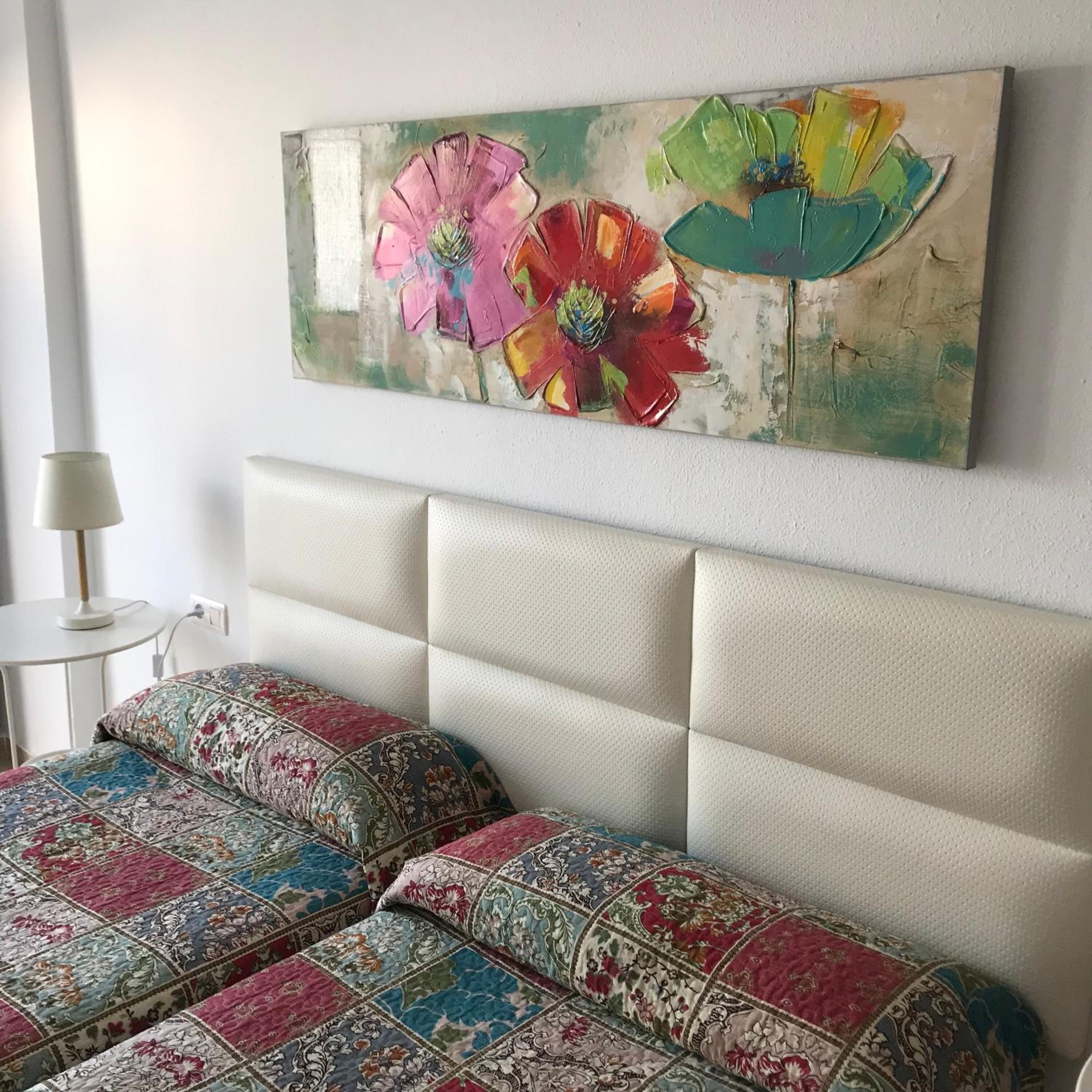 A bedroom with a white headboard, two beds with patterned bedding, and a colorful abstract painting on the wall.