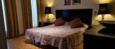 A hotel room with a large bed, two bedside tables with lamps, a headboard, and two framed pictures on the wall.