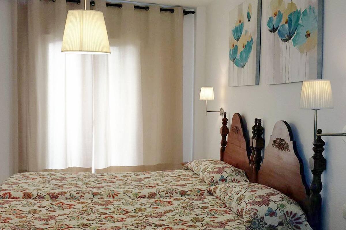 A bedroom with a floral bedspread, a wooden headboard, and two wall-mounted lamps.