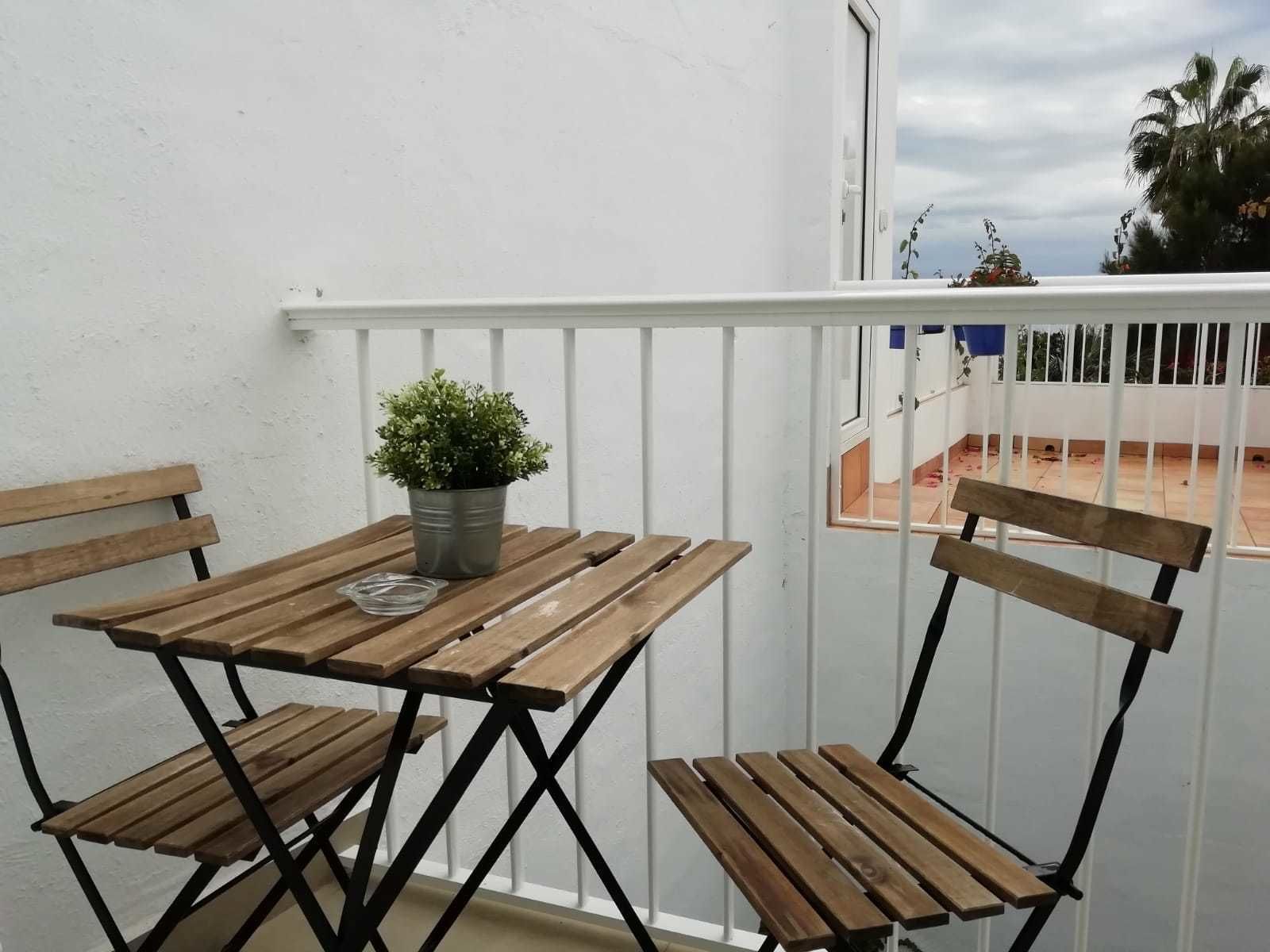 Un balcón con una mesa y sillas de madera, una planta en maceta y vistas del entorno.
