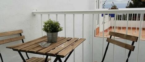 Un balcón con una mesa y sillas de madera, una planta en maceta y vistas del entorno.