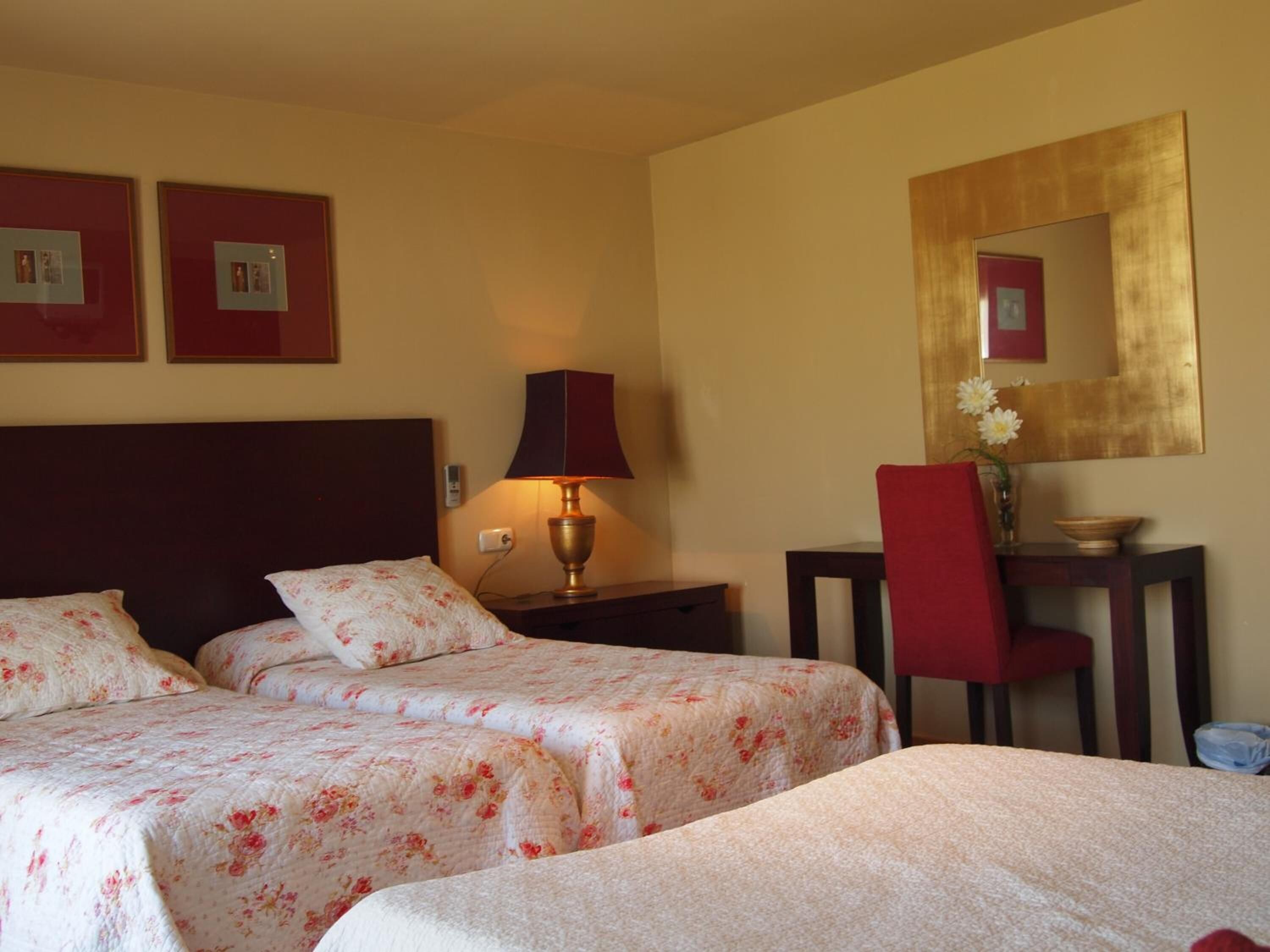 Habitación de hotel con dos camas, un escritorio, una silla, una lámpara y un espejo.