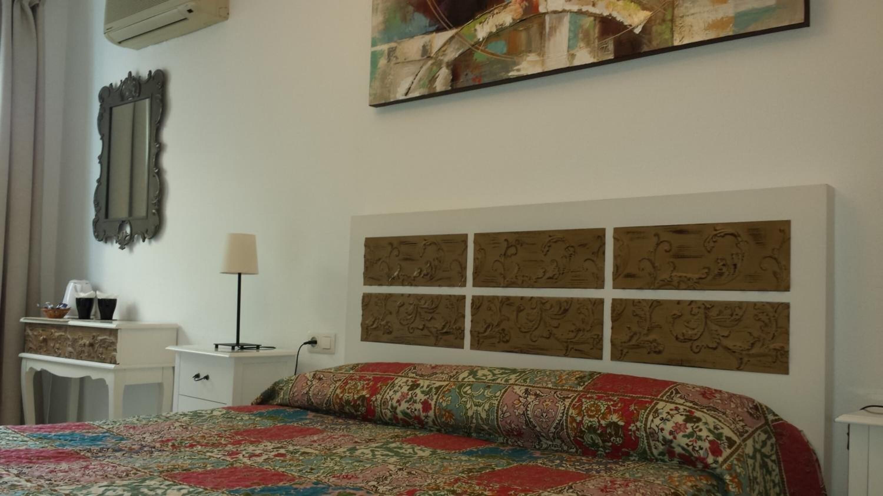 Un dormitorio con una cama grande, una mesita de noche, una lámpara, un espejo y una obra de arte en la pared.